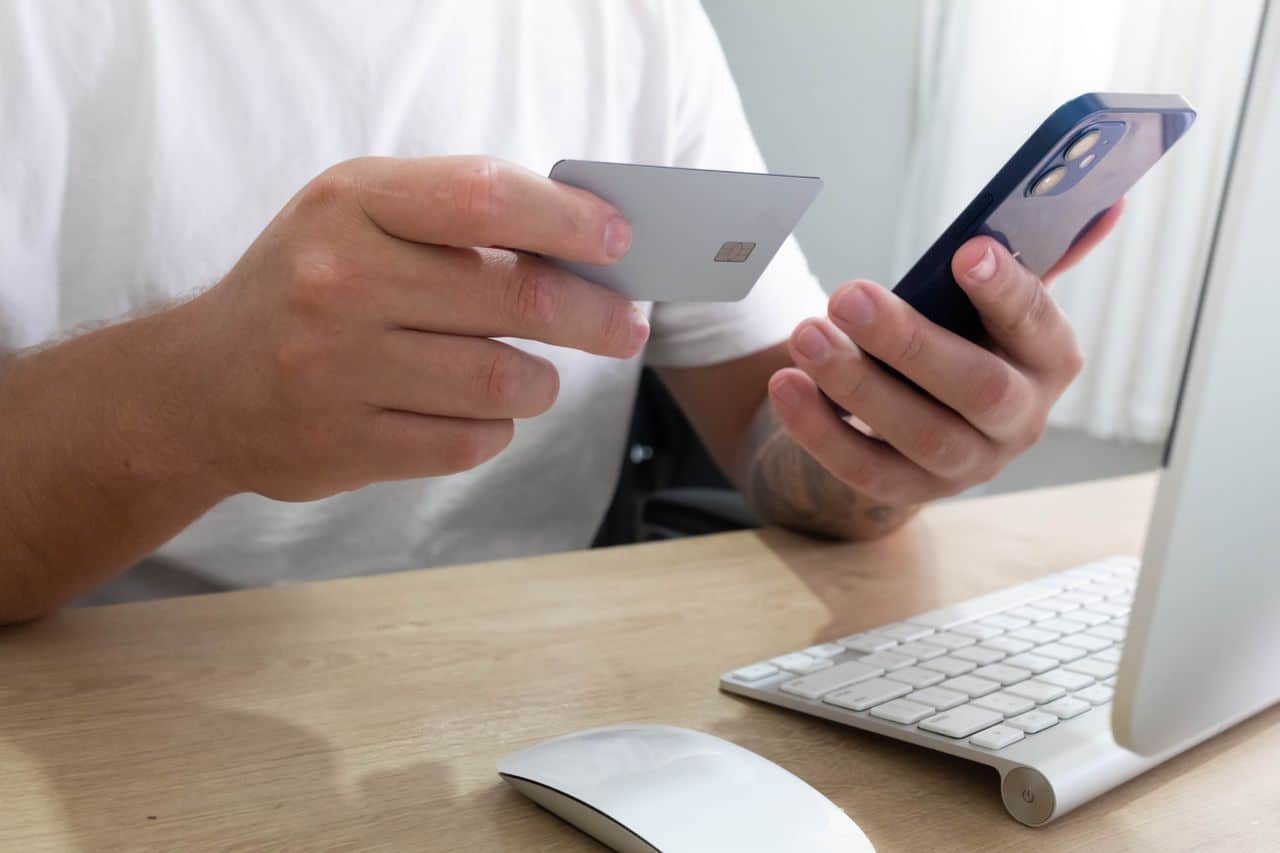 Person stellt eine digitale Kreditanfrage über das Smartphone, sitzend an einem modernen Arbeitsplatz